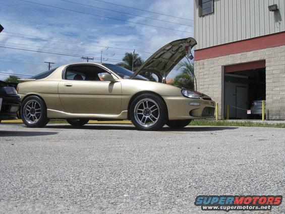 1994 Ford Probe coupe, gold, with hood open, parked outside a building
