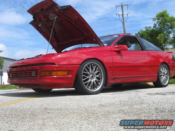 red coupe with hood open, aftermarket wheels, parked outside