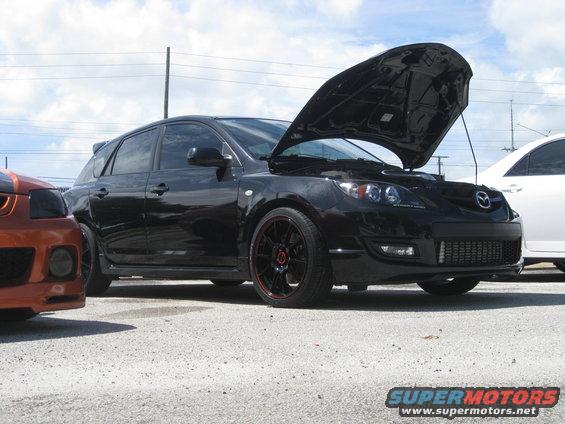 Black Mazda 3 hatchback with hood up, parked next to an orange car
