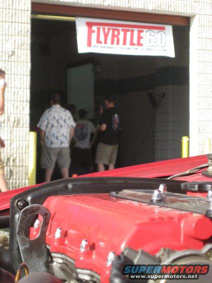 red engine cover with bolts, people in background under a banner that says FLYRTLE 6.0