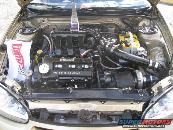 Mazda V6 DOHC 24-valve engine bay with aftermarket turbocharger and yellow Optima battery