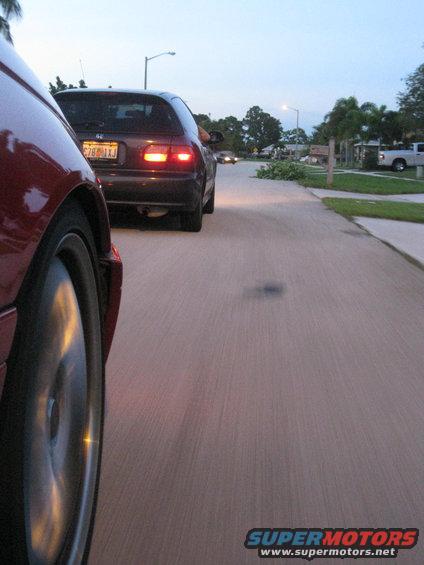 Red car front wheel and dark hatchback rear driving on street