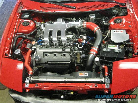 Red car engine bay with V6 engine, intake piping, and battery