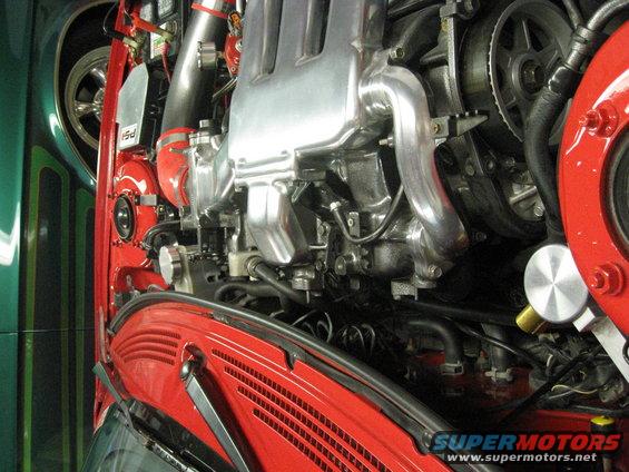 Engine bay with polished intake manifold, red fender, and green car fender. Supermotors.net watermark visible
