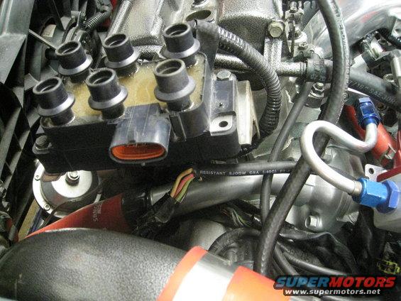 Engine ignition coil pack with spark plug wires connected. Some hoses and wiring are visible
