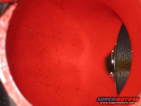 Close-up of a red oil filler neck with some debris in it and a black oil cap visible