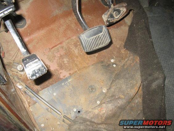 Close-up of rusty floorboard with clutch, brake, and accelerator pedals visible