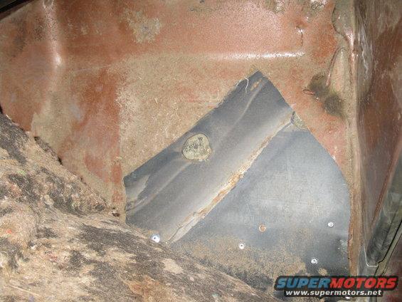Close-up of a vehicle's interior floor pan, showing rust and some insulation material