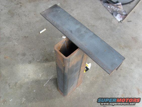 Metal channel resting on a rusty square tube on a concrete floor