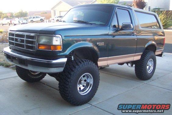 Green 1995 Ford Bronco with tan trim and large off-road tires, parked on a concrete driveway