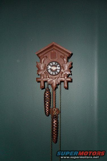 Brown cuckoo clock with pinecone weights hanging on a dark green wall