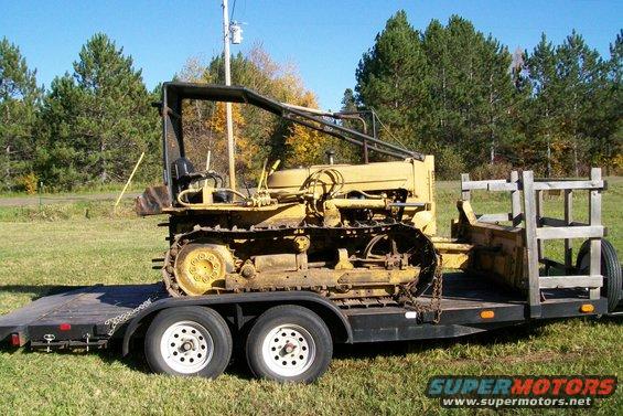 Yellow crawler tractor with a roll cage, loaded onto a dual-axle flatbed trailer