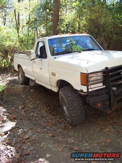 White 1987 Ford F-250 with large tires and exhaust stack on dirt path