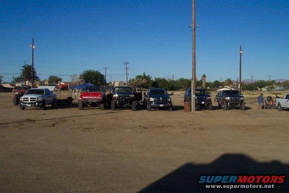 Several lifted trucks and SUVs parked in a dirt lot under a clear blue sky