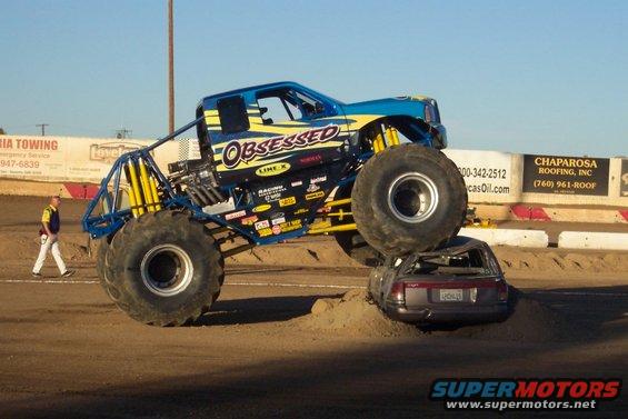 Monster truck with blue and yellow paint crushing a sedan