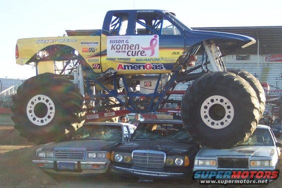 Monster truck with 'Susan G. Komen for the Cure' logo crushing several cars