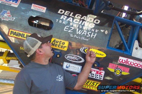Man looking up at a custom off-road vehicle covered in sponsor stickers like Delgado Racing and EZ Wash