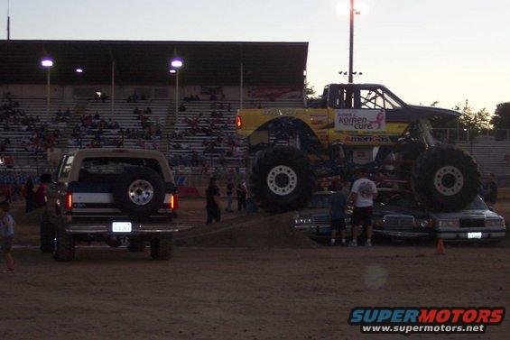 Tan Ford Bronco with spare tire on rear, facing away. Monster truck is to the right