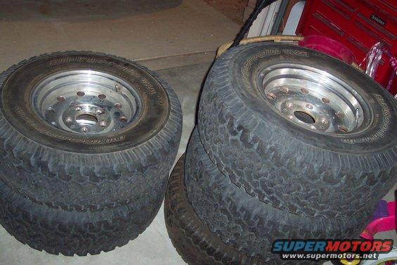 Four off-road tires on chrome rims stacked in a garage