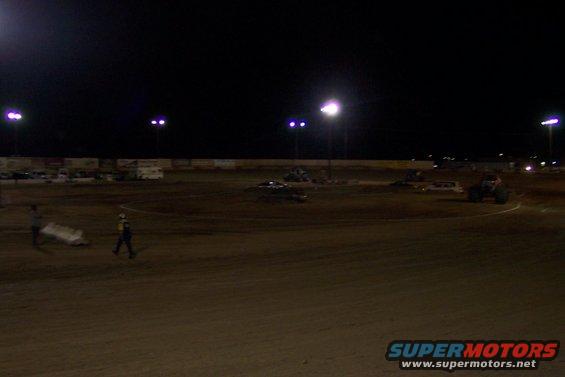 Dirt track at night with lights, vehicles, and people