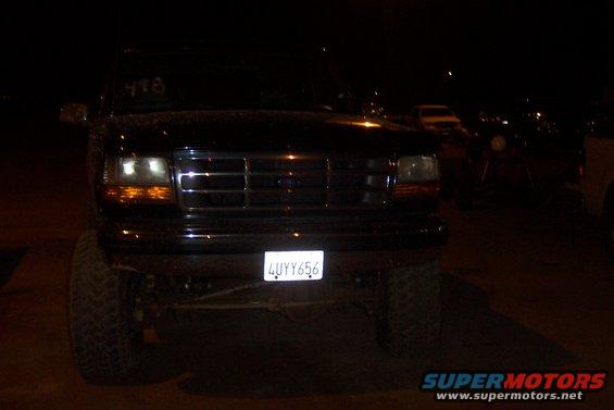 Black Ford Bronco front view at night. Large tires, chrome grille, and license plate 4UYY656 are visible
