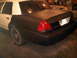 2003 Ford Crown Victoria - The rear of a two-tone Ford Crown Victoria shows a flat tire and a license plate.