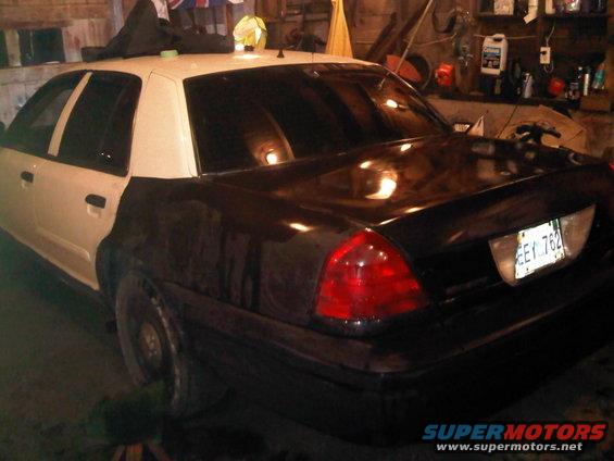 Black and white Ford Crown Victoria with a partial paint job, seen from the rear quarter