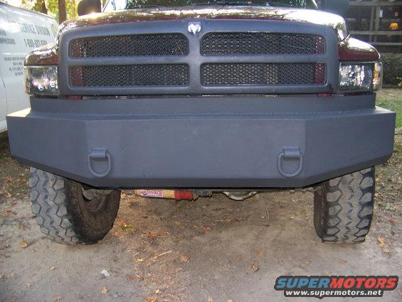 Front view of a dark red Dodge Ram truck with a custom gray bumper and tow hooks. The grille has the Dodge logo