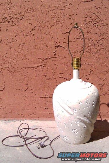 White textured lamp with a coiled cord and plug on a concrete surface against a reddish-brown wall