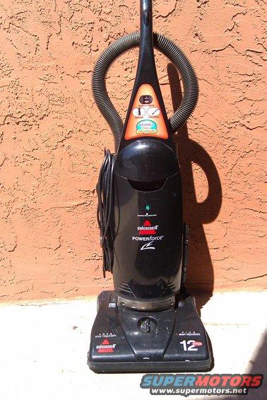 Black Bissell PowerForce vacuum cleaner leaning against a textured orange wall
