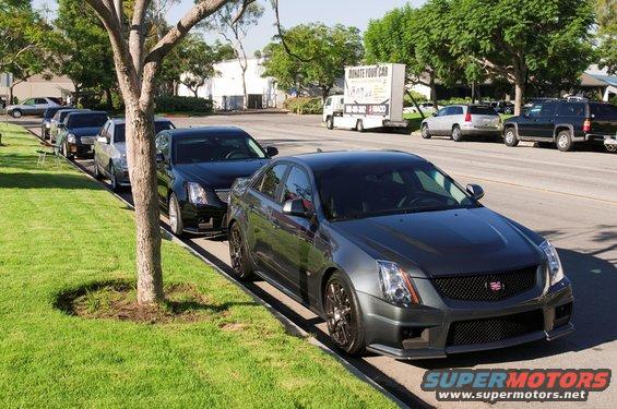 Dark gray Cadillac CTS-V parked on street, other Cadillacs in line behind it