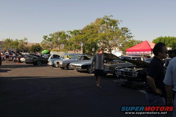 Several cars parked in a lot, some with hoods open, under a clear sky