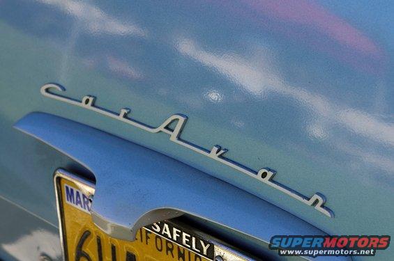 Chrome script emblem on light blue car body, partially obscuring California license plate