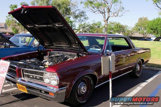 Maroon 1964 Pontiac GTO coupe, hood open, showing engine, parked in lot