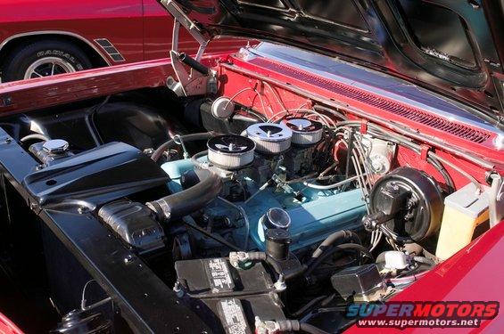 Engine bay with three carburetors and a red car in the background