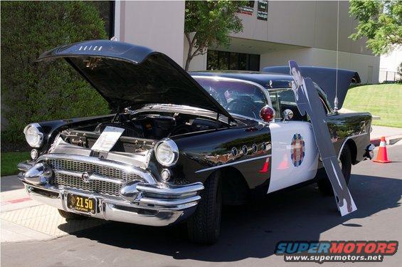 Black and white police car, hood open, showing engine. California license plate reads 21 50