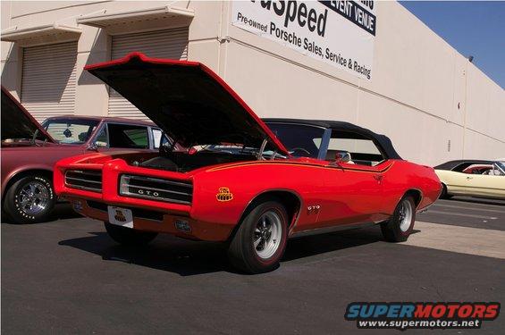 Red 1969 Pontiac GTO convertible with hood open, parked next to other cars