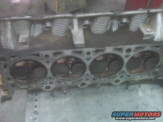 Close-up of an engine cylinder head with valves visible inside the cylinders
