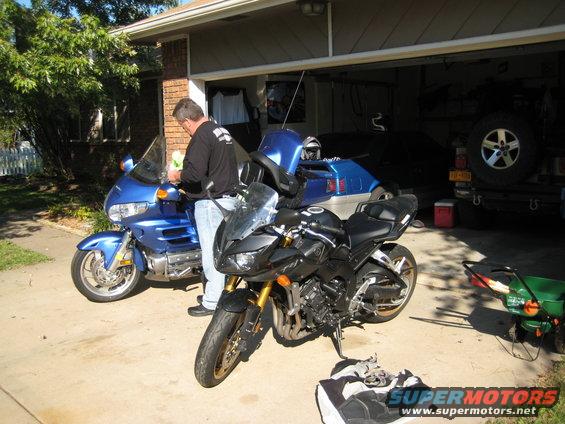 Man cleaning a blue motorcycle next to a black sportbike in a driveway