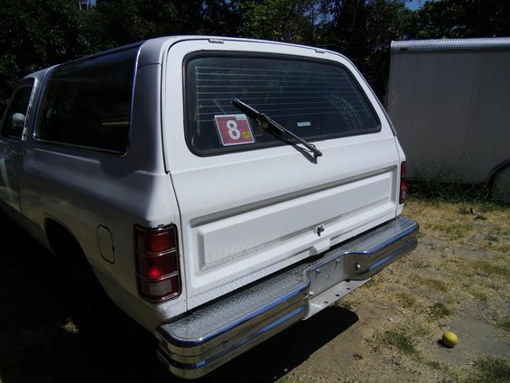 1987 Dodge 1500 SUV rear view, white with chrome bumper. Trailer visible to the right