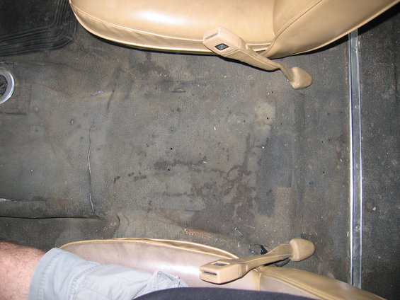 View of a dirty vehicle floor with tan seat belts and tan seats visible