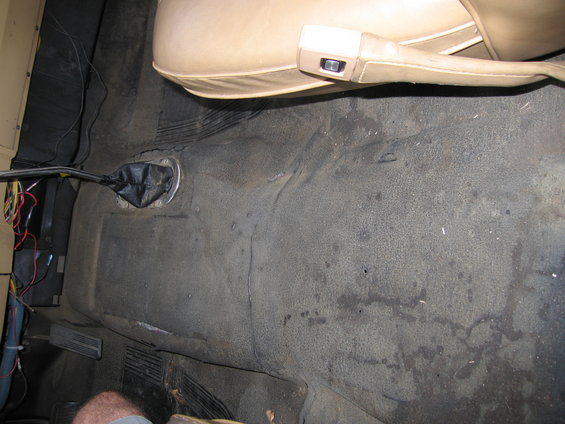 Tan seat and black floor mat in a vehicle interior with a manual shifter