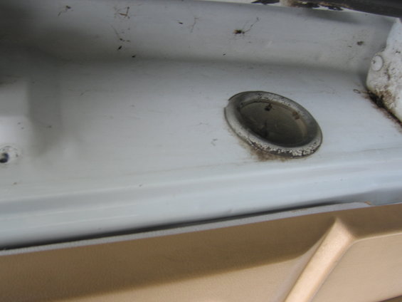 Close-up of a white interior door panel with a circular grommet and tan trim piece