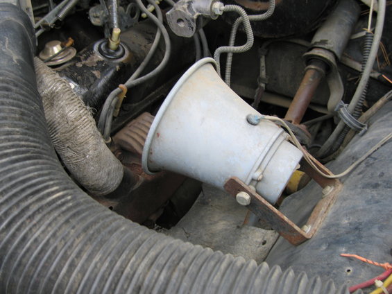 Engine compartment with a speaker mounted on rusty brackets. Visible parts include hoses, wires, and engine components