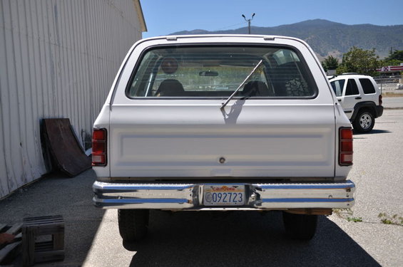 White SUV's rear, chrome bumper, California license plate C092723, parked next to a building