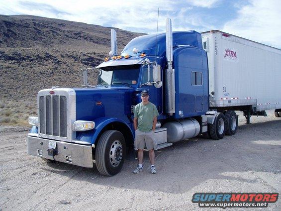 Blue Peterbilt 379 semi-truck with a man standing in front, pulling an XTRA Lease trailer