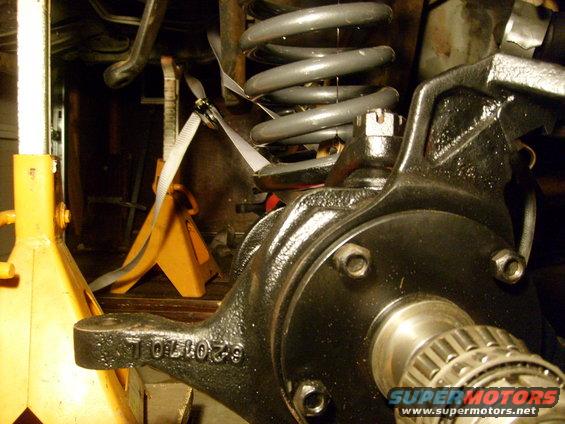 close-up of a vehicle's front suspension knuckle and coil spring, supported by jack stands