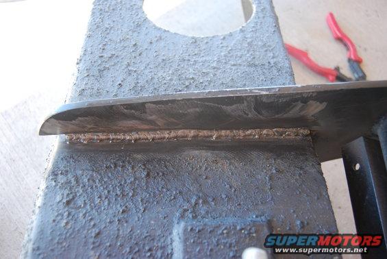 Welded metal part with red pliers in background