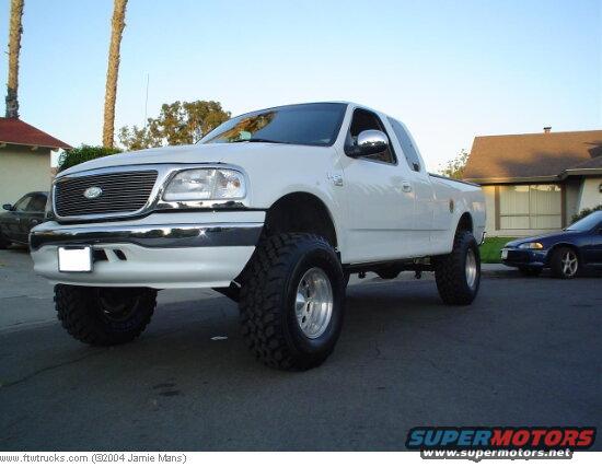 White lifted Ford F-150 pickup truck with aftermarket wheels and tires, parked on a residential street. A dark sedan is visible in the background