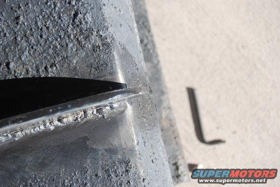 Close-up of a rough, textured metal part with visible welds and an L-shaped tool casting a shadow nearby